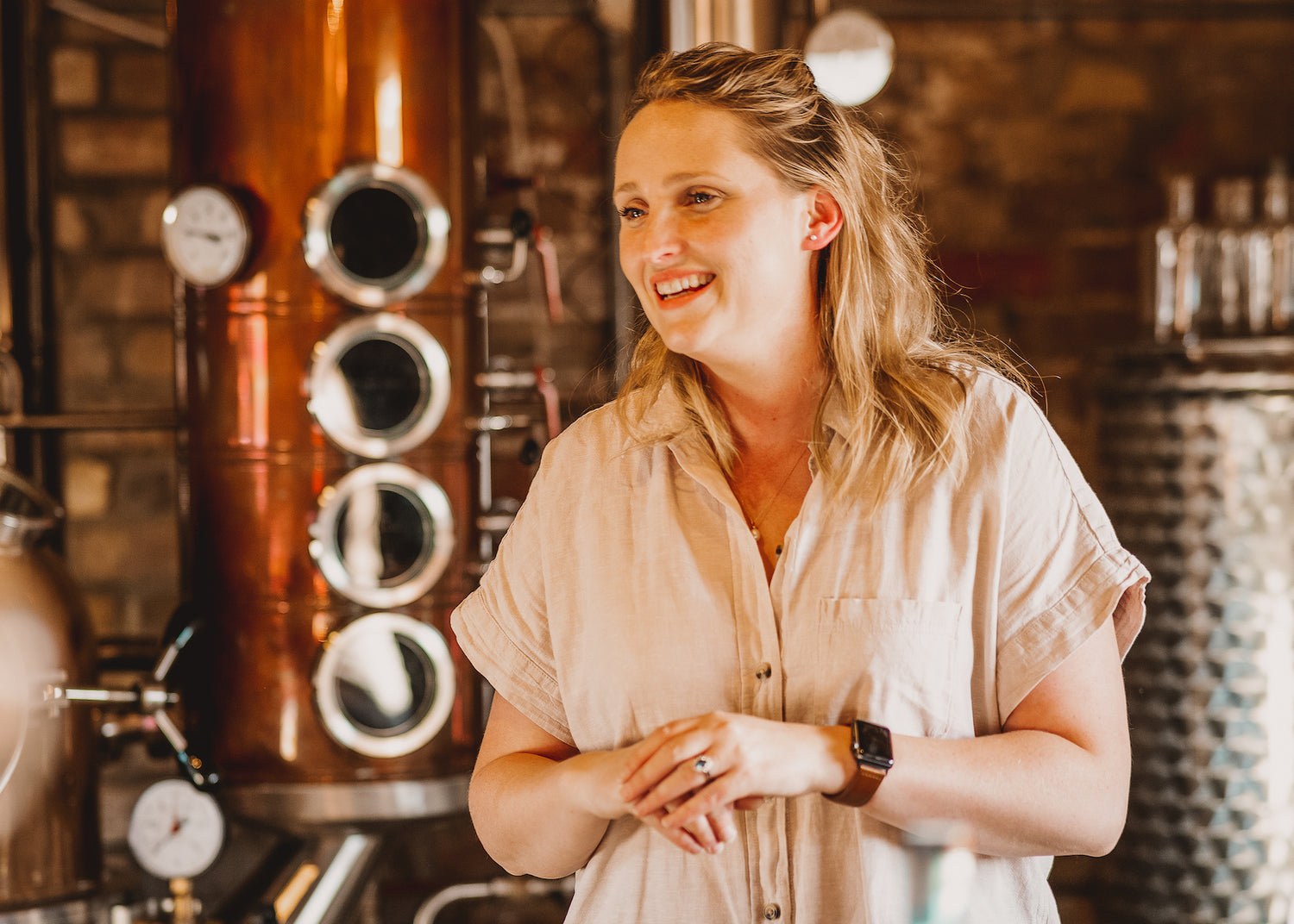 Emily stands in front of copper still and stainless steel tank, smiling whilst talking about the brand at Gin Discovery Session