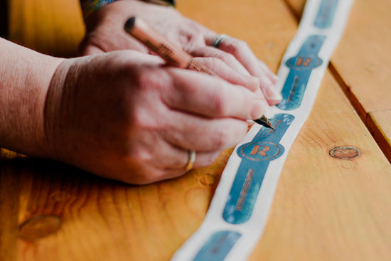Handwriting the batch numbers onto blue copper foiled labels 